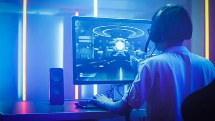 Wall Mural - Arc Shot of the Professional Gamer Playing in First-Person Shooter Online Video Game on His Personal Computer. He's Talking with His Team Through Headset. Room Lit by Neon Lights in Retro Arcade Style