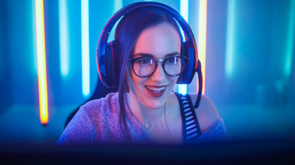 Wall Mural - Beautiful Friendly Pro Gamer Girl Does Video Game Gameplay stream, Wearing Headset Talks / Chats with Her Fans and Team into Headphones Microphone and Smiling. Background Cool Neon Retro Colors.