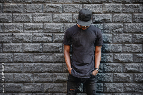Fotografía Handsome african american man in blank black t-shirt standing against brick wall