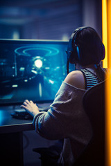 Wall Mural - Back View Shot of the Beautiful Professional Gamer Girl Playing in Online Video Game on Her PC. Casual Cute Geek Girl in Dark Room Lit by Neon Lights in Retro Arcade Style. Vertical Photo.