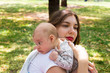 © Radoslav Cajkovic - Young mother caring her cute baby on the shoulder outside in the park during nice sunny day, Infant head resting on the shoulder in burping position, mom holding newborn