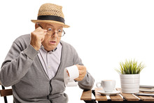Shocked Mature Man Seated At A Coffee Table Looking At The Bill