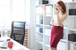 © Ivan Traimak - Beautiful young girl stands in the office near a shelf with documents.