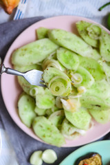 Woman hands tastes with fork green fresh cucumber salad with onion rings spices, herbs, garlic and unrefined oil. Raw vegan lunch, vegetarian healthy dinner