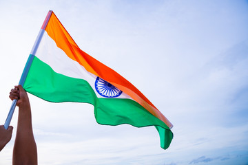 Close up man hand holding India flag on the blue sky background. Indian Independence Day, 15 August.