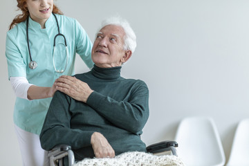 Wall Mural - Doctor with stethoscope supporting disabled senior man in the wheelchair in a hospital