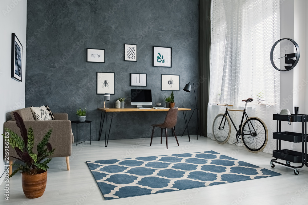 Patterned carpet in bright workspace interior with bicycle next to brown chair at desk. Real photo - obrazy, fototapety, plakaty 