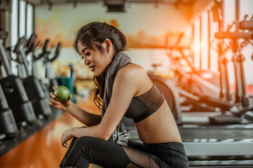 Athletic woman resting after working out in the gym.sitting on a treadmill and eating an apple.