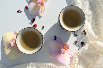 Tea ceremony on a white table. The table is decorated with orchids, dry berries and veil. Two cups with green tea.