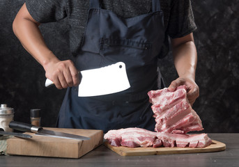 Wall Mural - Chef cook cuts large piece of pork meat on wooden cutting board with knife,concept of cooking