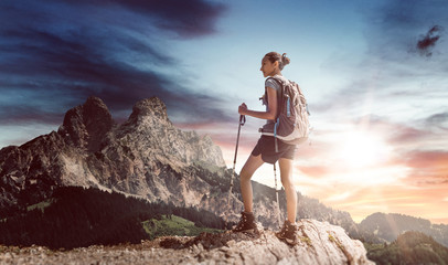 Wall Mural - young female hiker with walking sticks near ledge