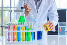 Hand Of Scientist Man Holding Yellow Color Glass Beaker Fill To Blue Color And Row Of Colorful Test Tube In A Laboratory. Concept Chemistry Medical Image.