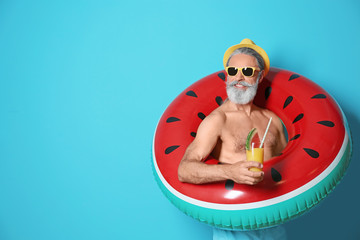 shirtless man with inflatable ring and glass of cocktail on color background