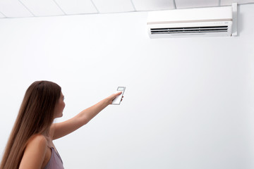 Canvas Print - woman operating air conditioner with remote control indoors