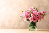 Vase with beautiful Eustoma flowers on table against color background