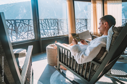 Cuadros en Lienzo Young man in a robe chilling on a open terrace in the SPA with an amazing mountains view during winter time