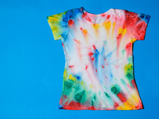 T-shirt painted in tie dye style on a blue background. Flat lay. Place for text.