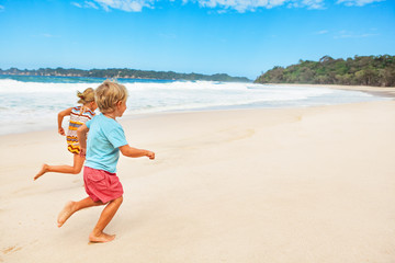 Happy barefoot kids have fun on beach walk. Run and jump by white sand along sea surf. Family travel lifestyle, outdoor sports activities and games. Summer vacation with children on tropical island