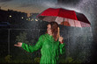 © Михаил Решетников - Young woman in green raincoat in rain with red umbrella at night. Smiling young woman in the rain with an umbrella in the evening. Beautiful woman with red umbrella in lanterns and rain drops