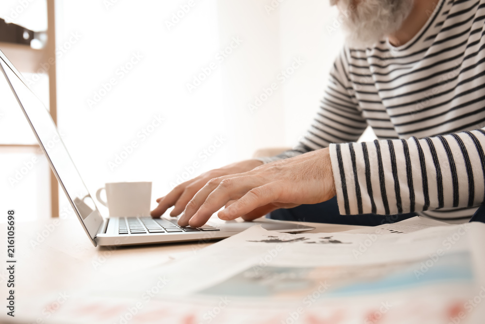 Senior man reading news on laptop screen at home