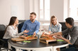 © Pixel-Shot - Young people eating pizza at table in office