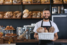 Male Baker Holding Wicker Basket With Fresh Bread In Shop