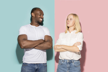 Closeup portrait of young couple, man, woman. One being excited happy smiling, other serious, concerned, unhappy on pink and blue background. Emotion contrasts