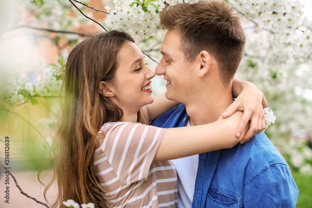 Happy young couple near blossoming tree in park on spring day