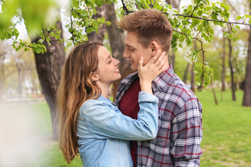 Wall Mural - Happy young couple near blossoming tree in park on spring day