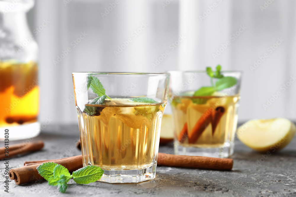 Apple drink with cinnamon in glass on table against light background