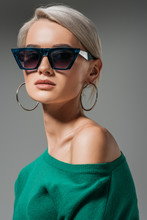 Attractive Female Model In Sunglasses And Green Sweater Looking At Camera Isolated On Grey Background