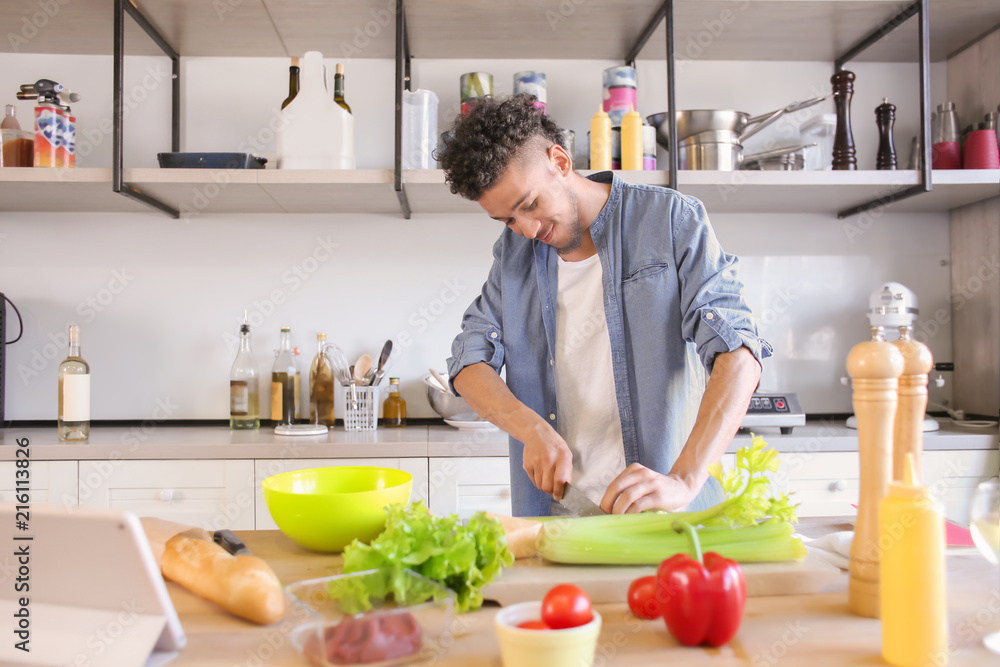 Young African-American man cooking in kitchen