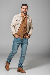 Poster - handsome man posing in corduroy shirt and autumn jacket with hands in pockets of jeans, on grey