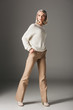 © LIGHTFIELD STUDIOS - elegant blonde woman posing in white sweater and beige pants, on grey