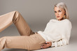 © LIGHTFIELD STUDIOS - elegant blonde woman lying in white sweater and beige pants, on grey