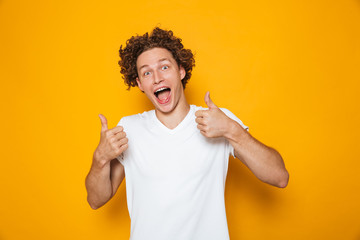 Poster - Handsome happy man 20s with brown curly hair shouting and showing thumbs up on camera, isolated over yellow background