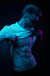 © monchak - Neon light portrait of sexy muscular man in yellow glasses, pulling up t-shirt, showing abs