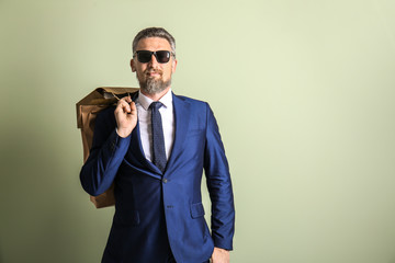 Handsome mature man in suit with shopping bags on color background