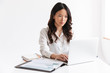 © Drobot Dean - Photo of young asian woman with long dark hair sitting at table and working with documents and laptop, isolated over white background in studio