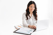 © Drobot Dean - Photo of successful asian woman with long dark hair sitting at table and working with documents and laptop, isolated over white background in studio