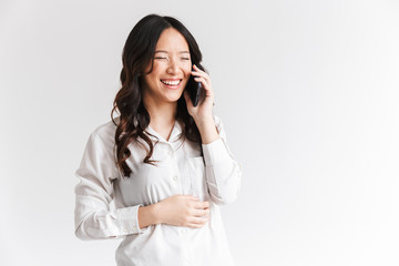 Wall Mural - Image of brunette chinese woman with long dark hair holding and talking on cell phone, isolated over white background in studio