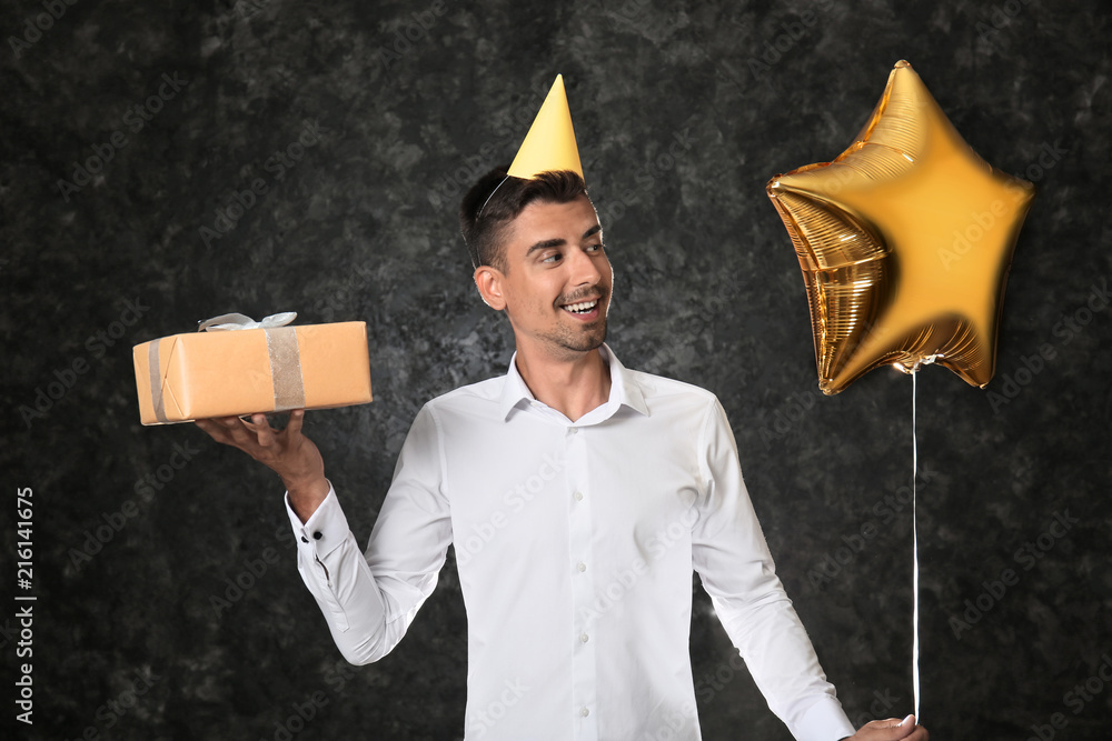 Young man with birthday present and balloon on dark background