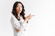 © Drobot Dean - Asian woman with long dark hair looking at camera with beautiful smile and pointing finger aside at copyspace text or product, isolated over white background in studio