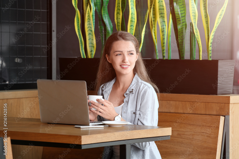 Young female freelancer drinking coffee while working on laptop in cafe