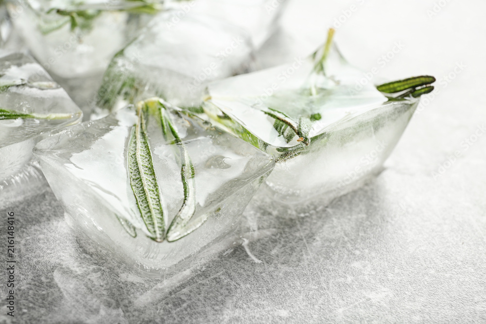 Rosemary frozen in ice cubes on light grey background, closeup