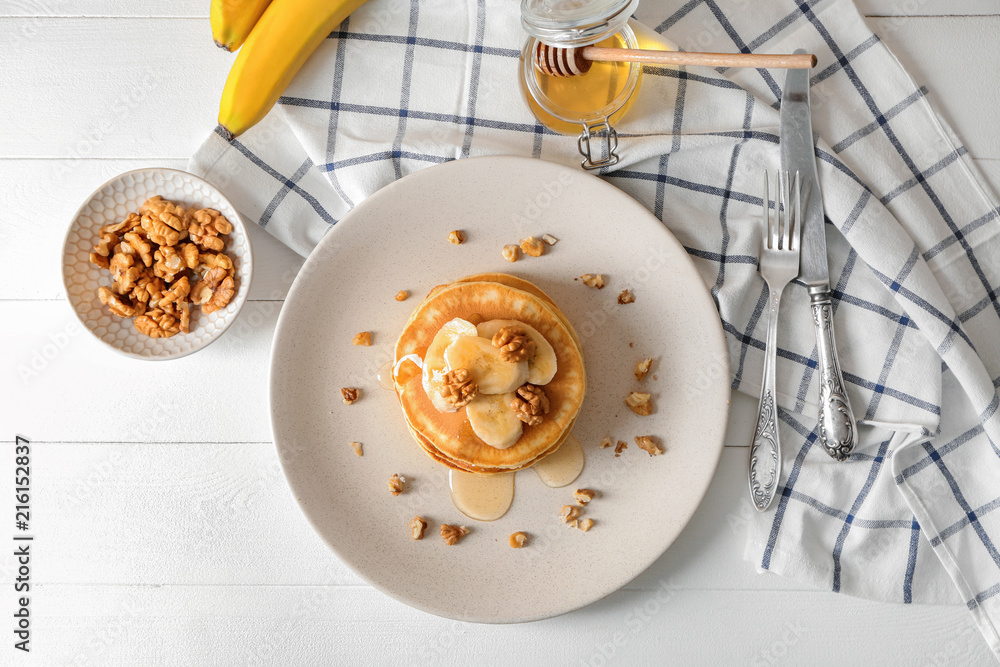 Plate with tasty pancakes, walnuts and sliced banana on table