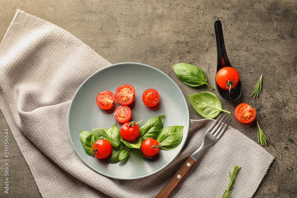 Plate with ripe cherry tomatoes and herbs on grey background