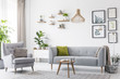 Creative, wooden pendant light above a gray sofa and a comfy armchair in a scandinavian living room interior with a gallery of botanic drawings