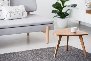 cup on a wooden coffee table and blurry foreground with graphic pillows on a gray sofa in a white li