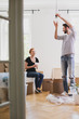 © Photographee.eu - Man is hanging a lamp while furnishing new home with smiling wife